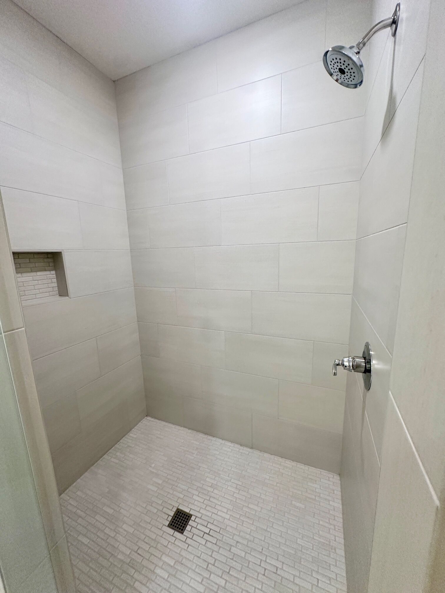 Un espacio de ducha pequeño y cerrado, con azulejos blancos y cabezal de ducha.