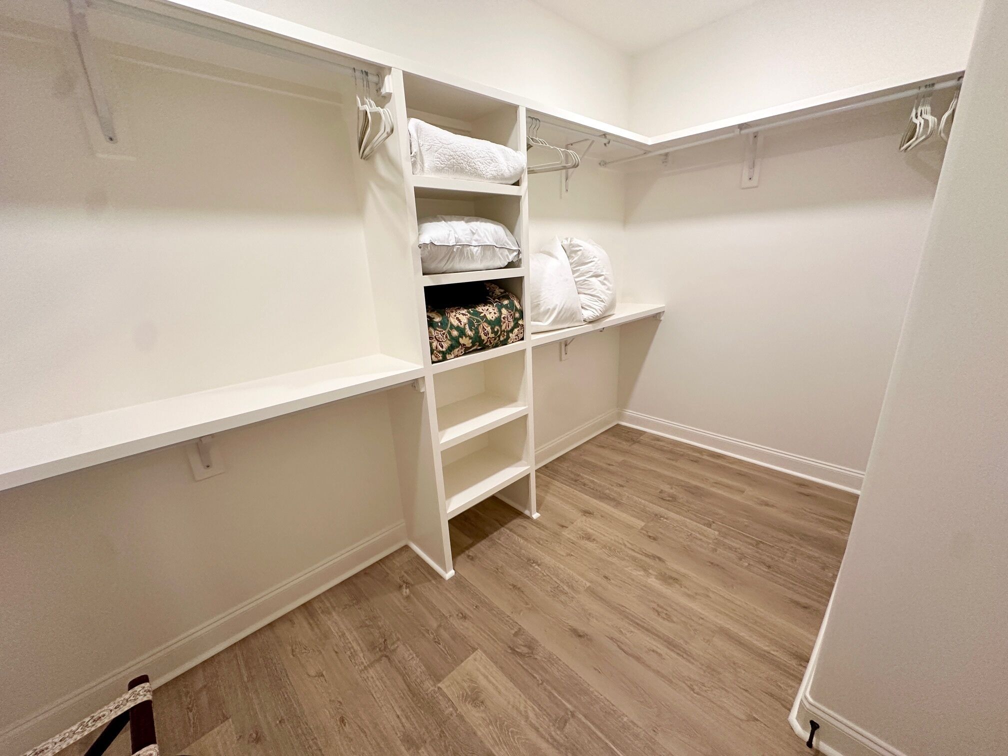 A walk-in closet with white shelving, a wooden floor, and hanging space.