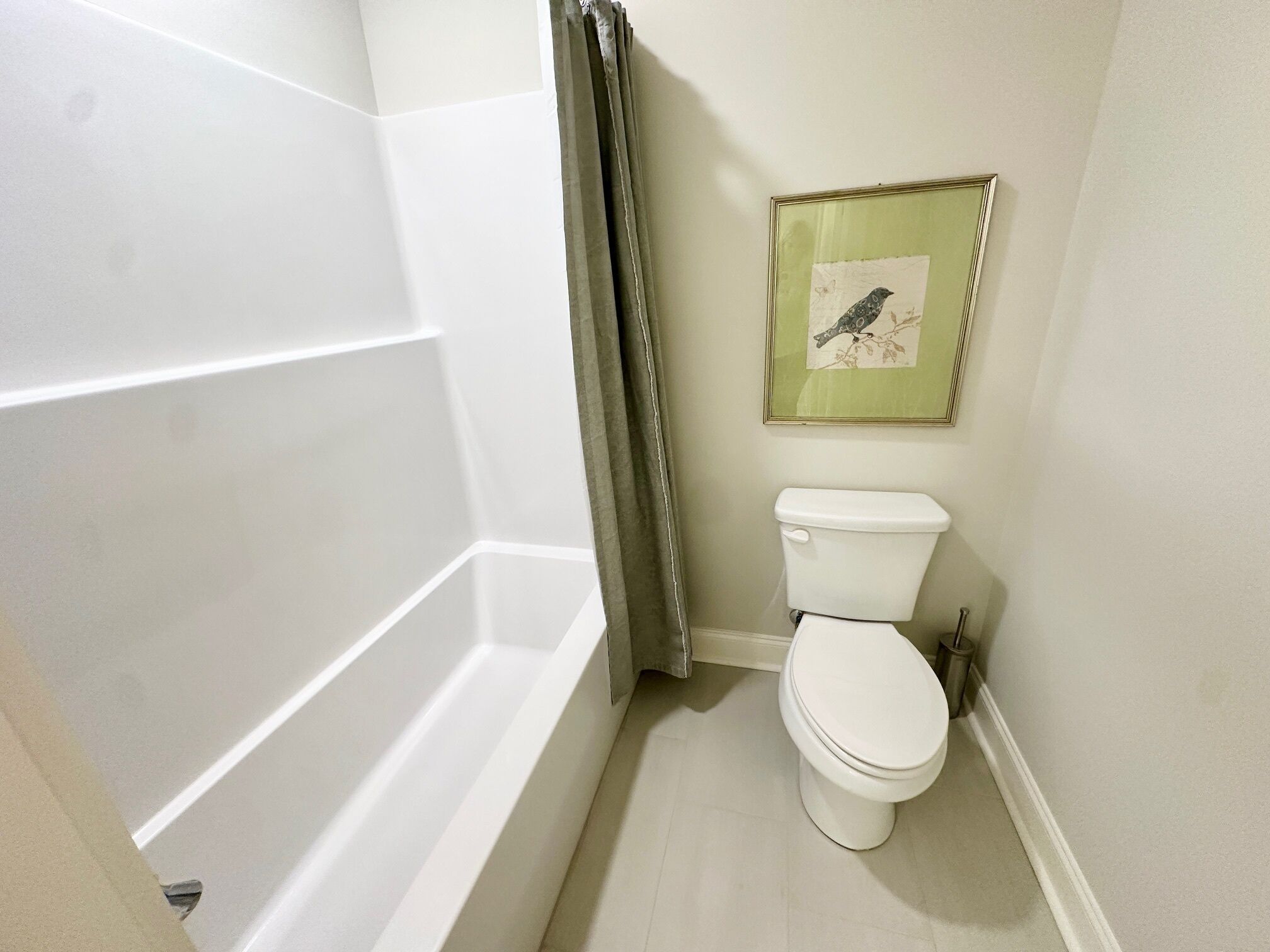 Een badkamer met een witte badkuip, een toilet en een gepresenteerd schilderij van een vogel aan de muur.