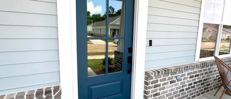 A blue front door with a welcome mat, a brick wall, and a porch with a chair.