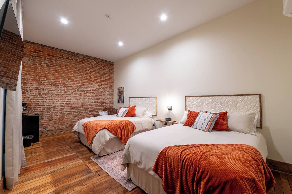 A room with two beds, a brick wall, and a wooden floor.
