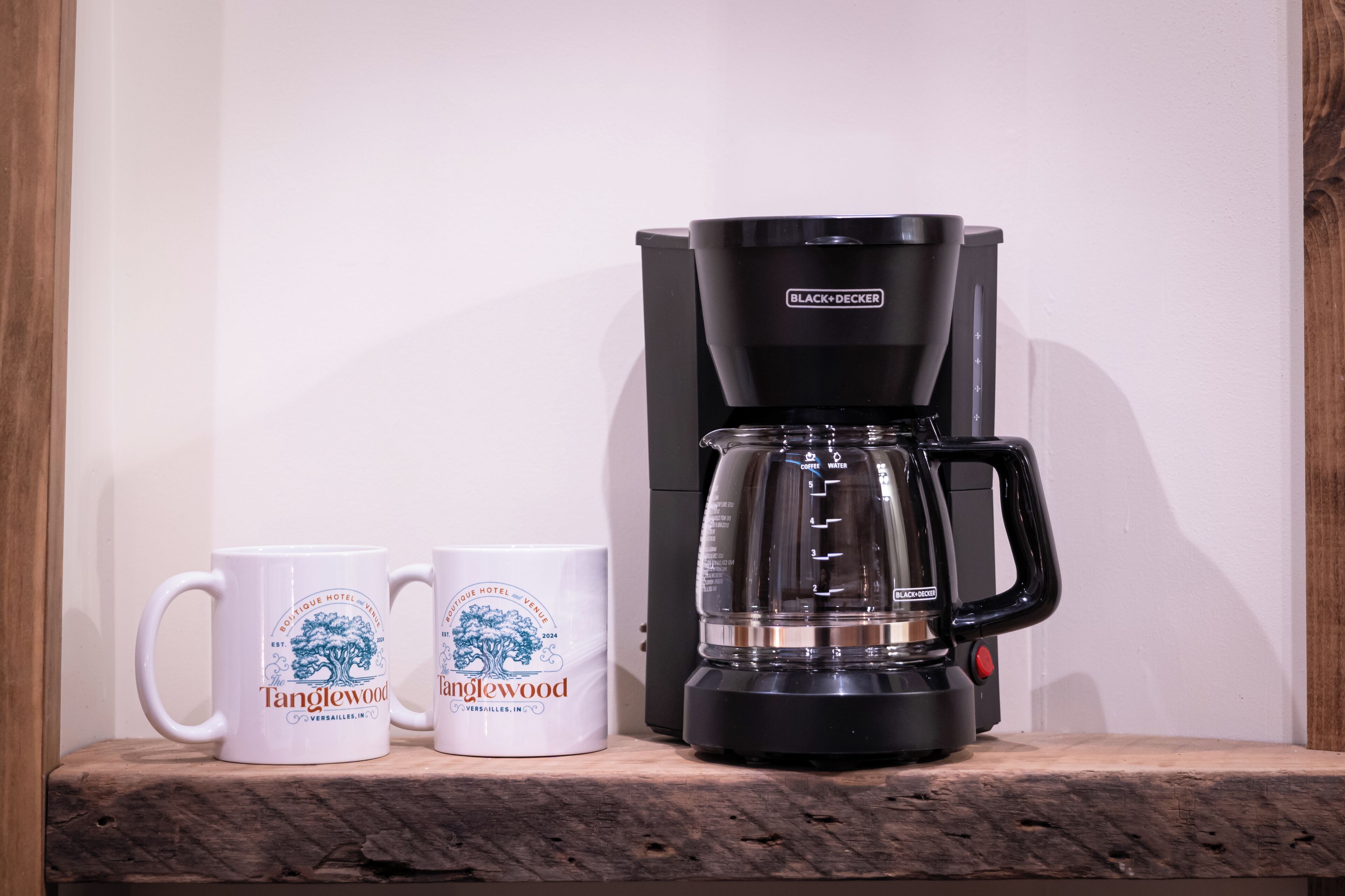 Een koffiezetapparaat en twee mokken op een houten plank.