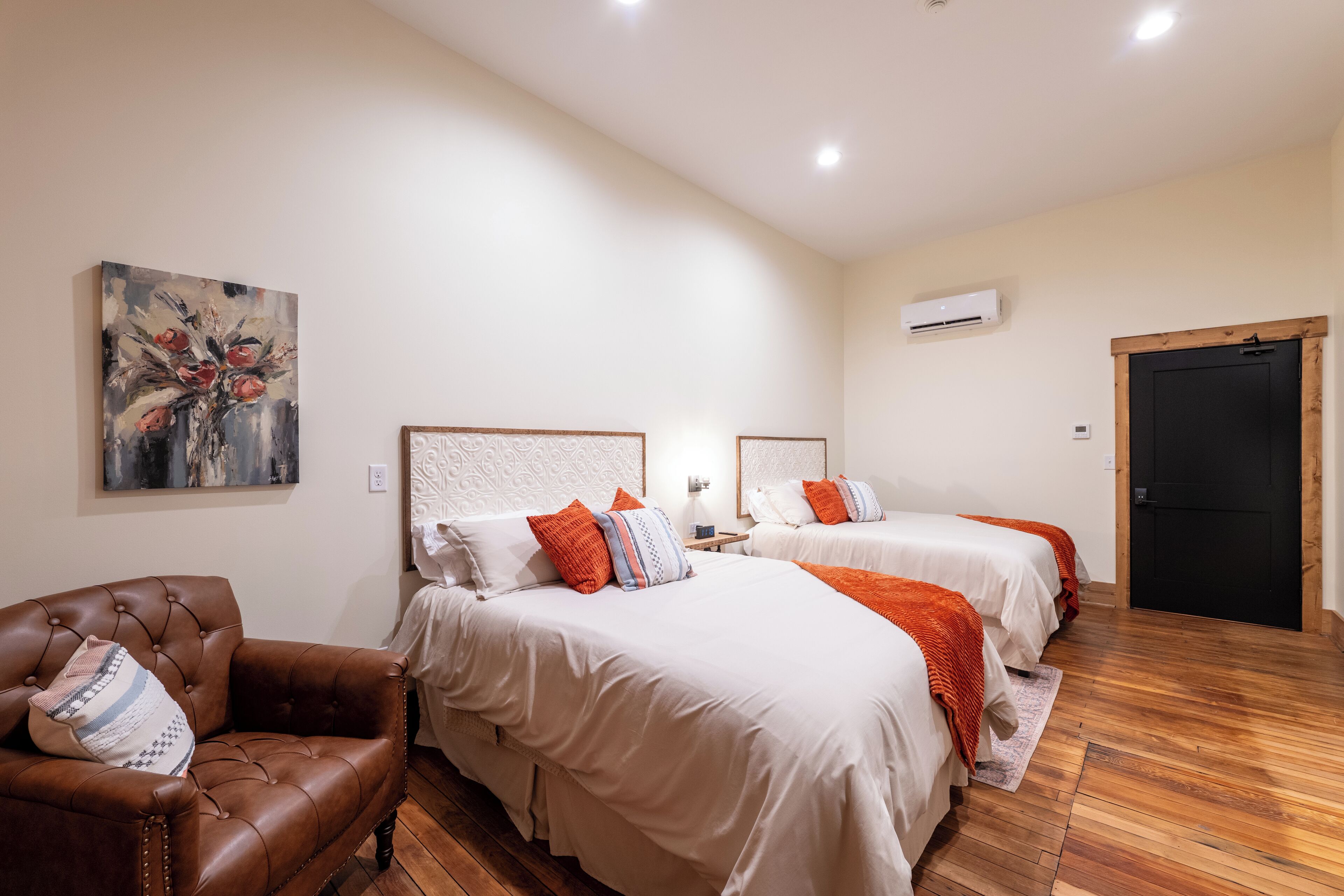 Una habitación de hotel con dos camas, un sillón de cuero marrón y un cuadro en la pared.