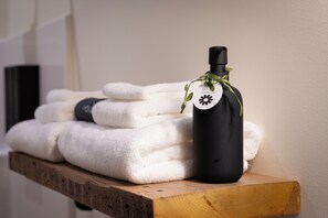 A wooden shelf with neatly folded white towels and a black bottle with a label, possibly containing a bath product, tied with a green ribbon. - The Tanglewood (Versailles)