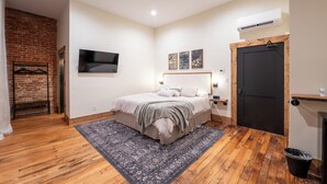 Ein Schlafzimmer mit Bett, Holzboden, Backsteinwand, Fernseher und einer Tür.