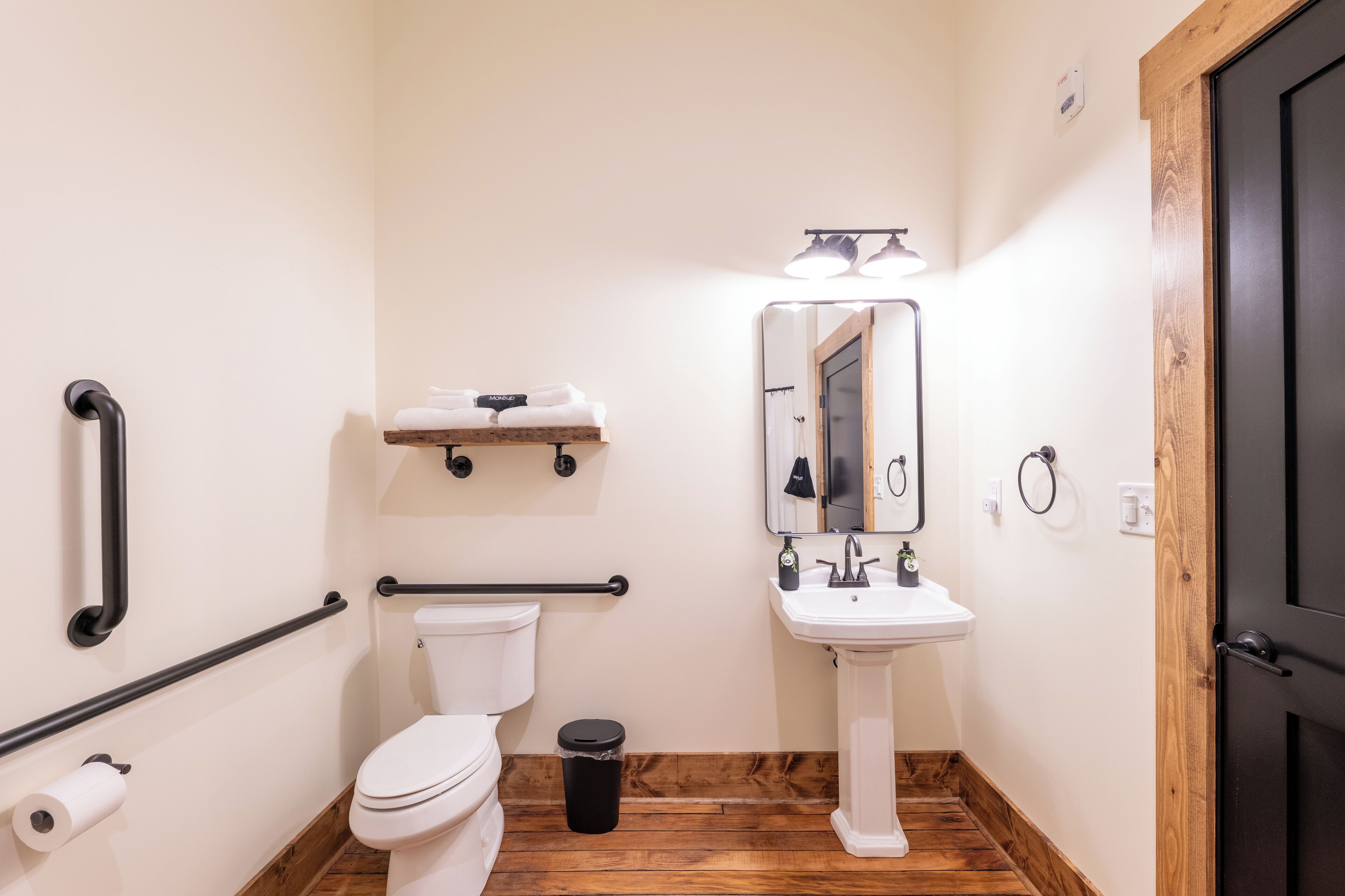 A bathroom with a toilet, sink, mirror, and handrails.