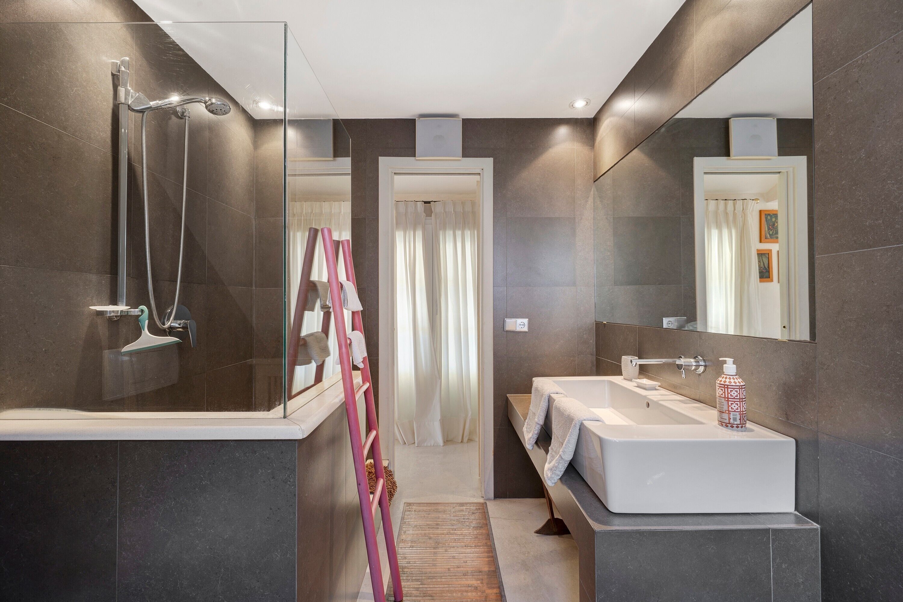 A modern bathroom with a glass shower enclosure, a white sink, and a large mirror.