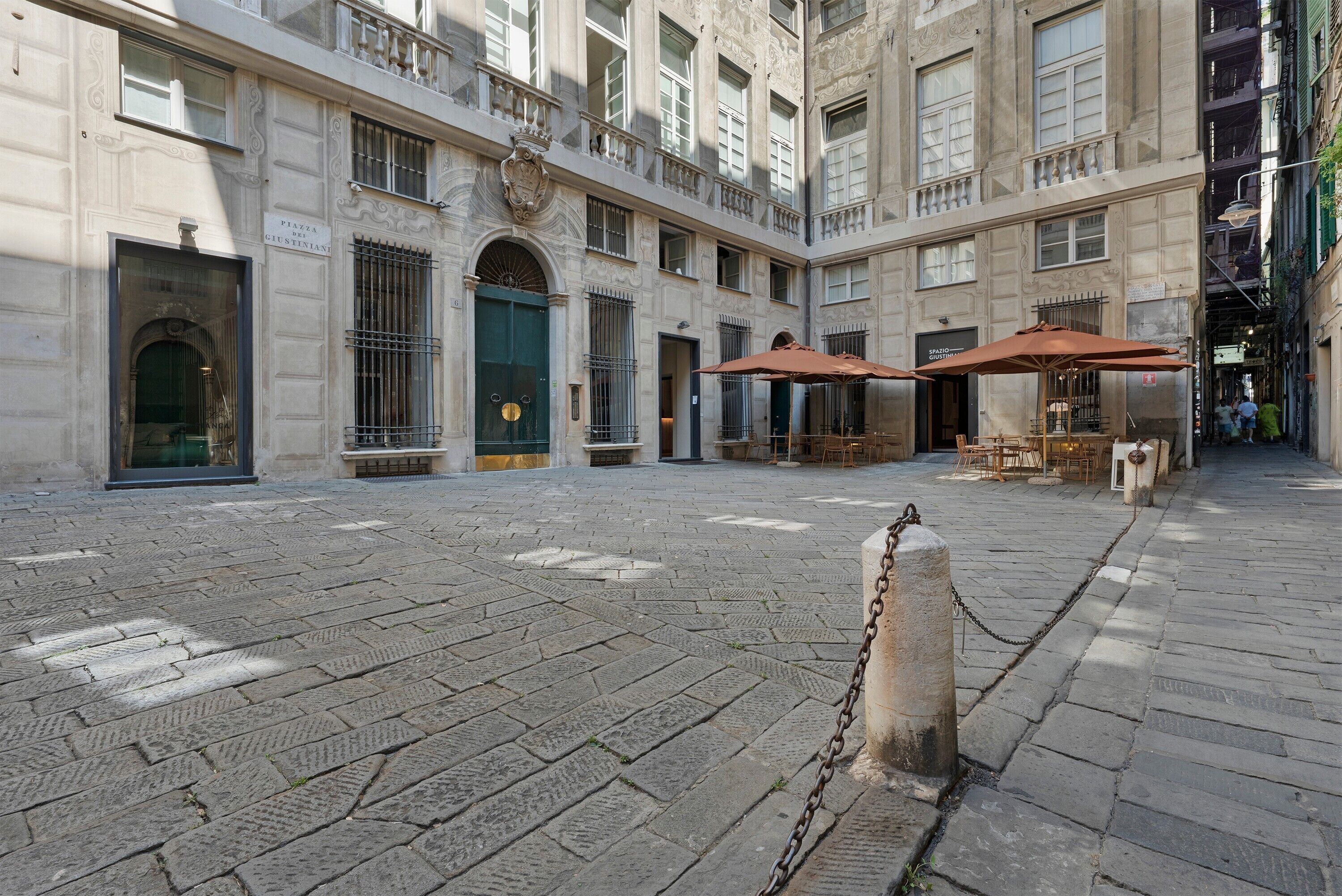 A courtyard with stone paving, a chain barrier, and outdoor seating with umbrellas.