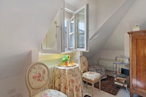 Une petite pièce agréable, avec un plafond en pente, un radiateur, une table avec des chaises et une bibliothèque.
