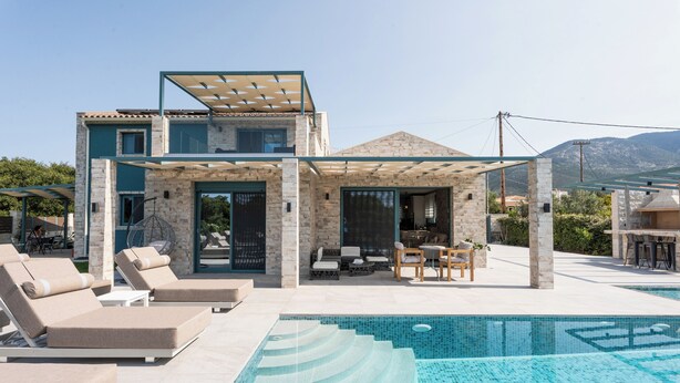Een modern huis met een zwembad, terras en uitzicht op bergen.