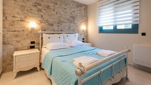 Een slaapkamer met een wand met baksteenmotief, een bed met een blauwe quilt, witte kussens en een nachtkastje met een lamp.