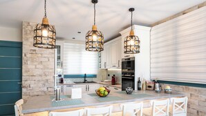 Een moderne keuken met een centraal eiland, hanglampen en een accentmuur van steen.