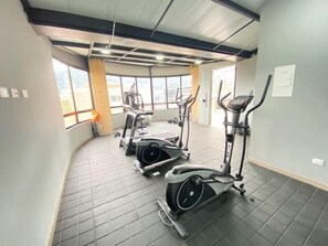 Une salle de sport équipée de machines de cardio, avec un mur en briques et de grandes fenêtres.