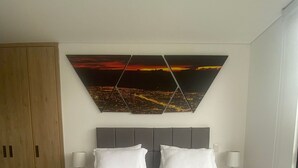 A hotel room with a large bed, two bedside tables, a headboard, and a cityscape painting on the wall. - Edificio Benyalt 94 (Bogota)