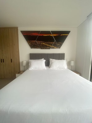 A hotel room with a large bed, two bedside tables, a headboard, and a cityscape painting on the wall. - Edificio Benyalt 94 (Bogota)