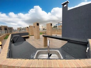 Une terrasse sur le toit équipée d’un évier, d’un espace barbecue et de piliers en briques.