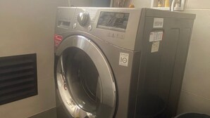 A front-loading washing machine in a laundry room with a vent, a trash bin, and a window. - Edificio Benyalt 94 (Bogota)