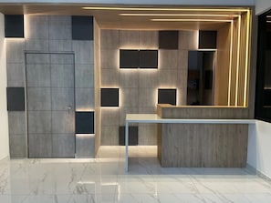 Un área de recepción moderna con suelo de mármol, un mostrador de recepción y una pared decorativa de madera con paneles iluminados.