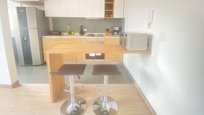 A modern kitchen with white cabinets, a built-in microwave, a gas stove, and two bar stools. - Edificio Benyalt 94 (Bogota)