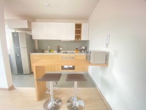 A modern kitchen with white cabinets, a built-in microwave, a gas stove, and two bar stools. - Edificio Benyalt 94 (Bogota)