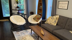 A modern living room with a dark wood floor, a grey sofa, two white armchairs, a wooden coffee table, and a large window with curtains. - Charming 2BR near Lake Barkley – fully equipped and ready for your stay! (Grand Rivers)