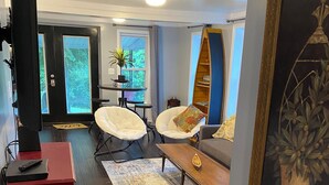 A living room with dark wooden flooring, a red cabinet, two white armchairs, a wooden coffee table, and a large framed painting. - Charming 2BR near Lake Barkley – fully equipped and ready for your stay! (Grand Rivers)