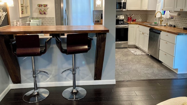 A modern kitchen with a wooden island, two bar stools, stainless steel appliances, and white cabinetry. - Charming 2BR near Lake Barkley – fully equipped and ready for your stay! (Grand Rivers)