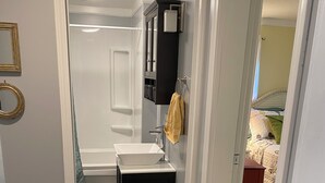 A narrow hallway leading to a bathroom with a white sink, a black cabinet, and a towel hanging on the wall. - Charming 2BR near Lake Barkley – fully equipped and ready for your stay! (Grand Rivers)