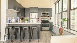 Une cuisine moderne avec des meubles de couleur sombre, des appareils en acier inoxydable et une grande fenêtre donnant sur la ville.