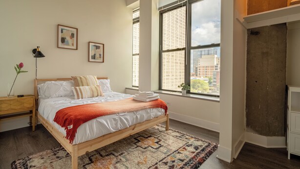 Une chambre avec un grand lit, une fenêtre donnant sur la ville et un plancher en bois.