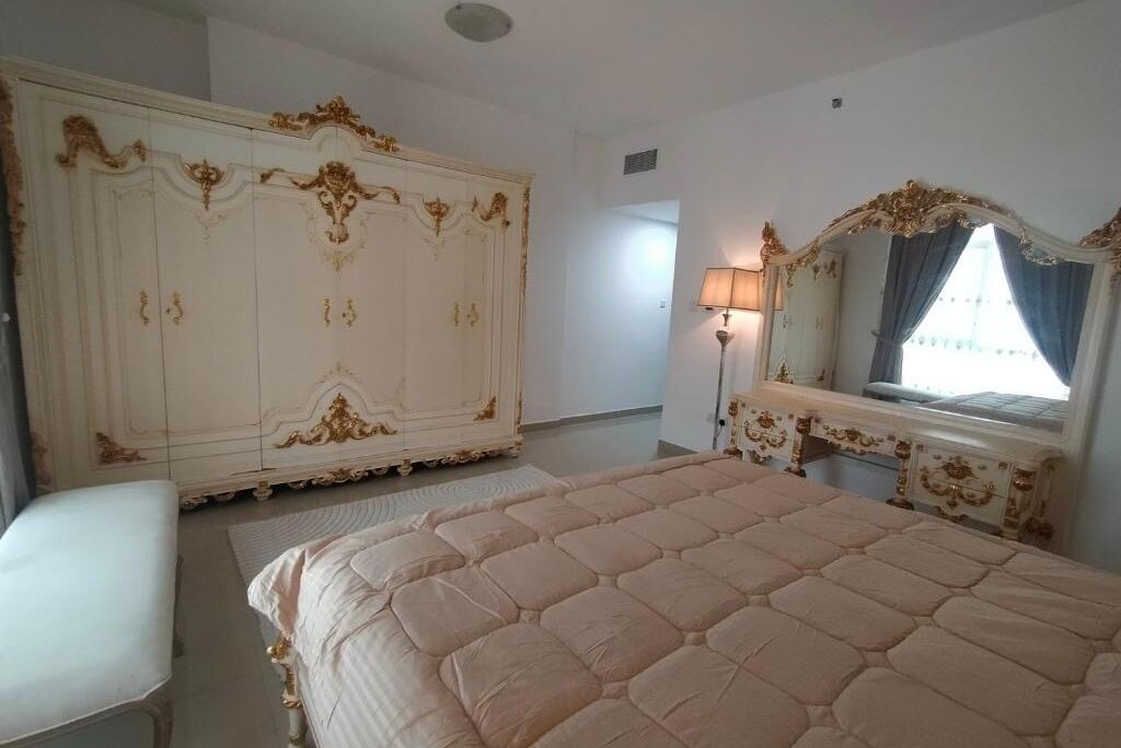 A bedroom with a large bed, a wardrobe, a dressing table, and a mirror.