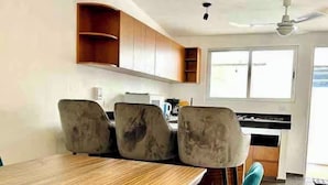 A dining area with a wooden table and four chairs, a ceiling fan, and a window with blinds.