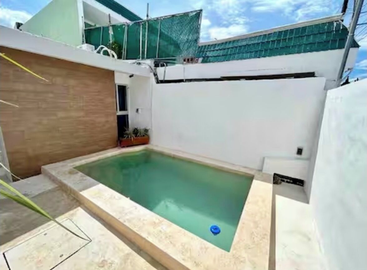 A rectangular swimming pool with a blue floatation device, surrounded by a beige tiled deck.