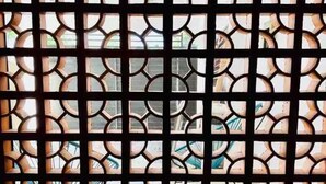A window with a geometric pattern, likely a security screen, and a view of a building outside.