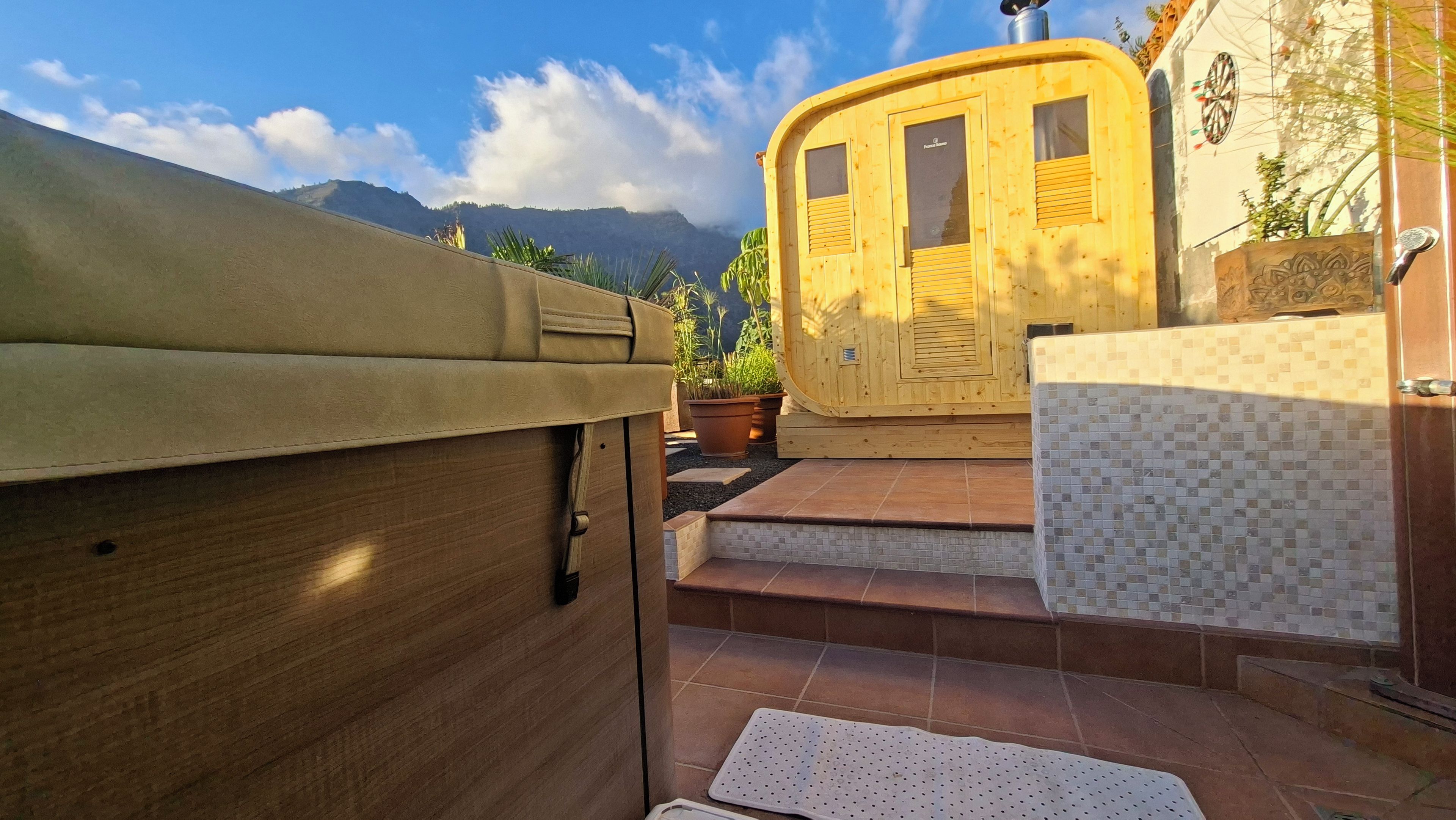 A wooden structure with a door and windows, a tiled area with steps, and a view of mountains in the background.