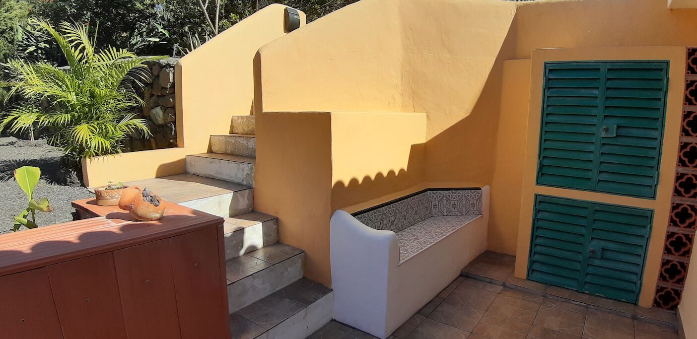 A small outdoor area with a set of stairs leading to a white bench with a patterned cushion.