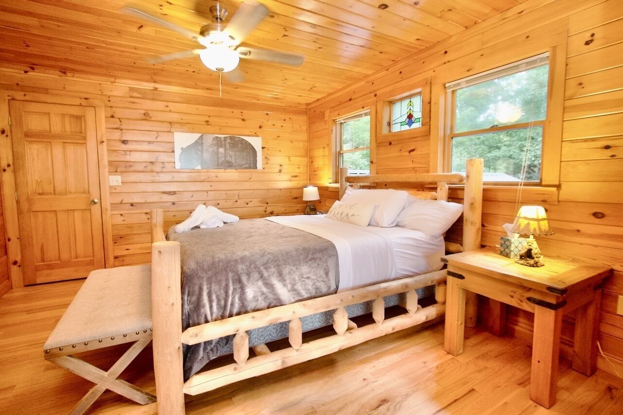 A wooden cabin bedroom with a bed, bench, nightstand, and a ceiling fan.
