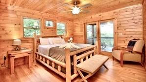 Een slaapkamer in een houten blokhut met een bed, een bankje, een stoel en een plafondventilator.