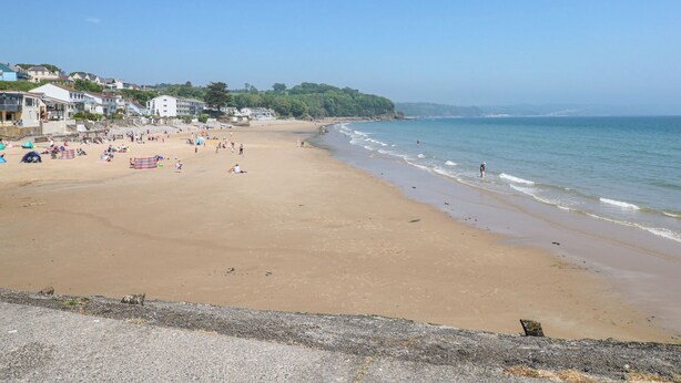 Ein weiter Sandstrand mit blauem Himmel, wenigen Personen und Gebäuden im Hintergrund.