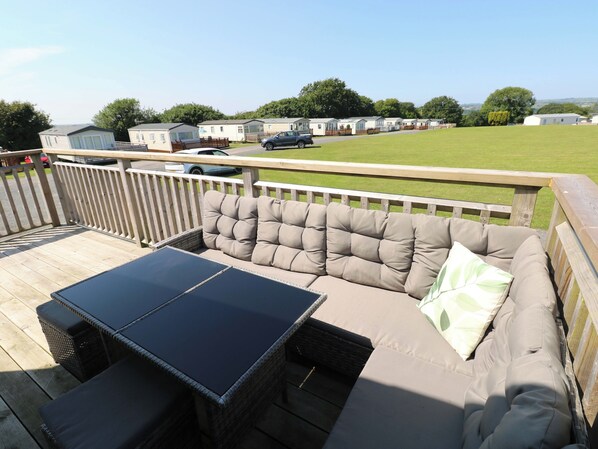 A deck with a sofa and a table, overlooking a grassy area with mobile homes in the background.