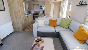 Ein modernes Wohnzimmer mit einer grauen Couch, einem kleinen weißen Couchtisch und einer Küche im Hintergrund.