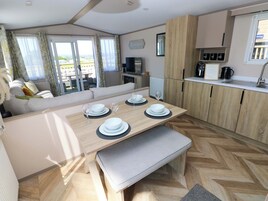 A modern kitchen with wooden cabinets, a dining area with a bench, and a view of the outdoors through large windows.