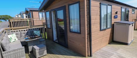 A wooden cabin with a deck, furnished with a sofa and a table.