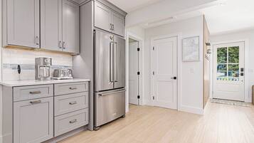 A modern kitchen with grey cabinets, a stainless steel refrigerator, and a coffee maker.