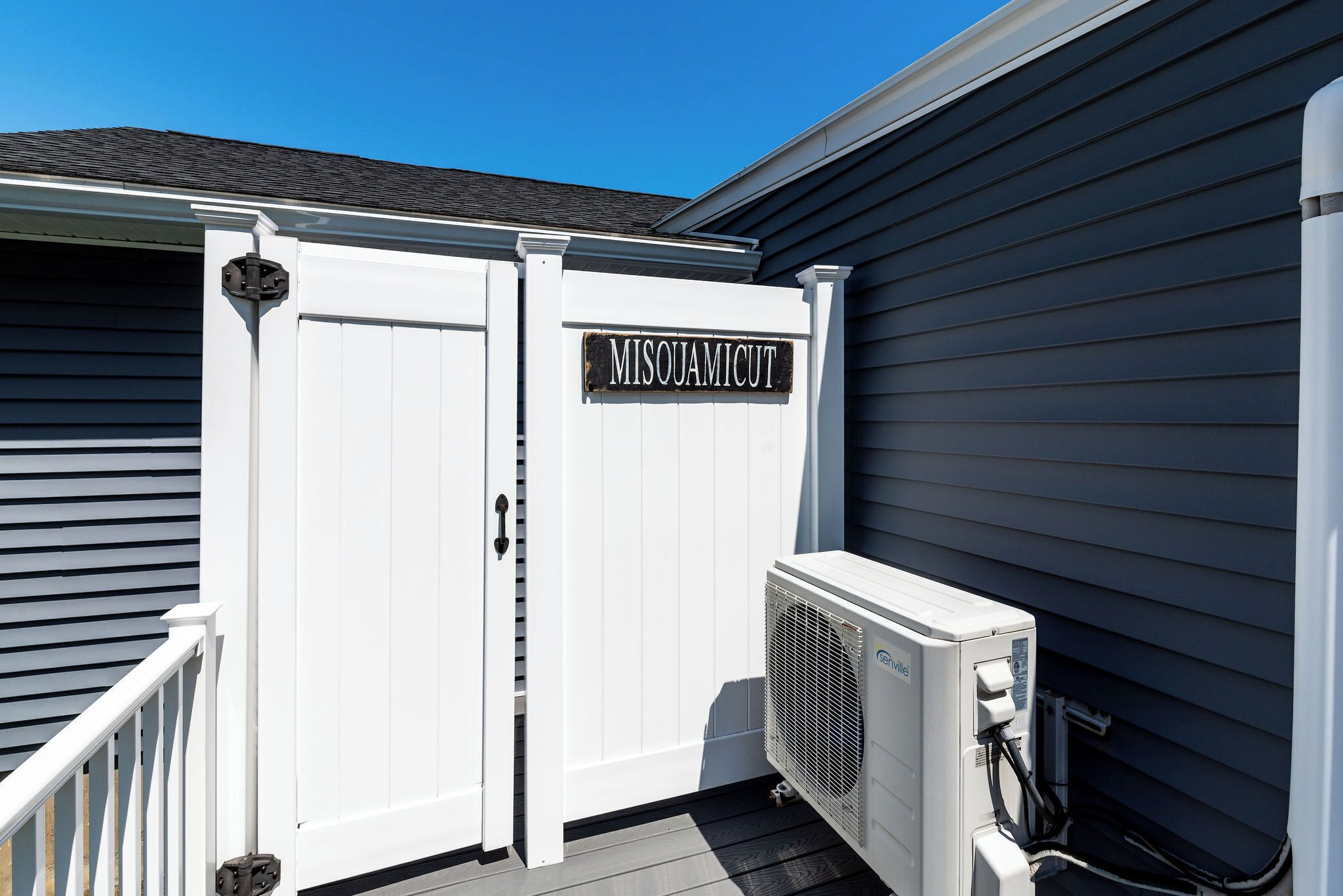 A white outdoor unit with a sign reading "MISQUAMICUT" attached to a building with dark siding.