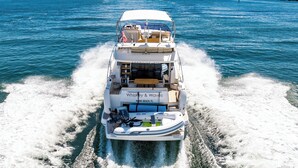 A boat named "Whiskey & Waves" with a covered deck, seating area, and a flag. - Amazing 3 bedrooms luxury yacht in North Miami (North Miami)
