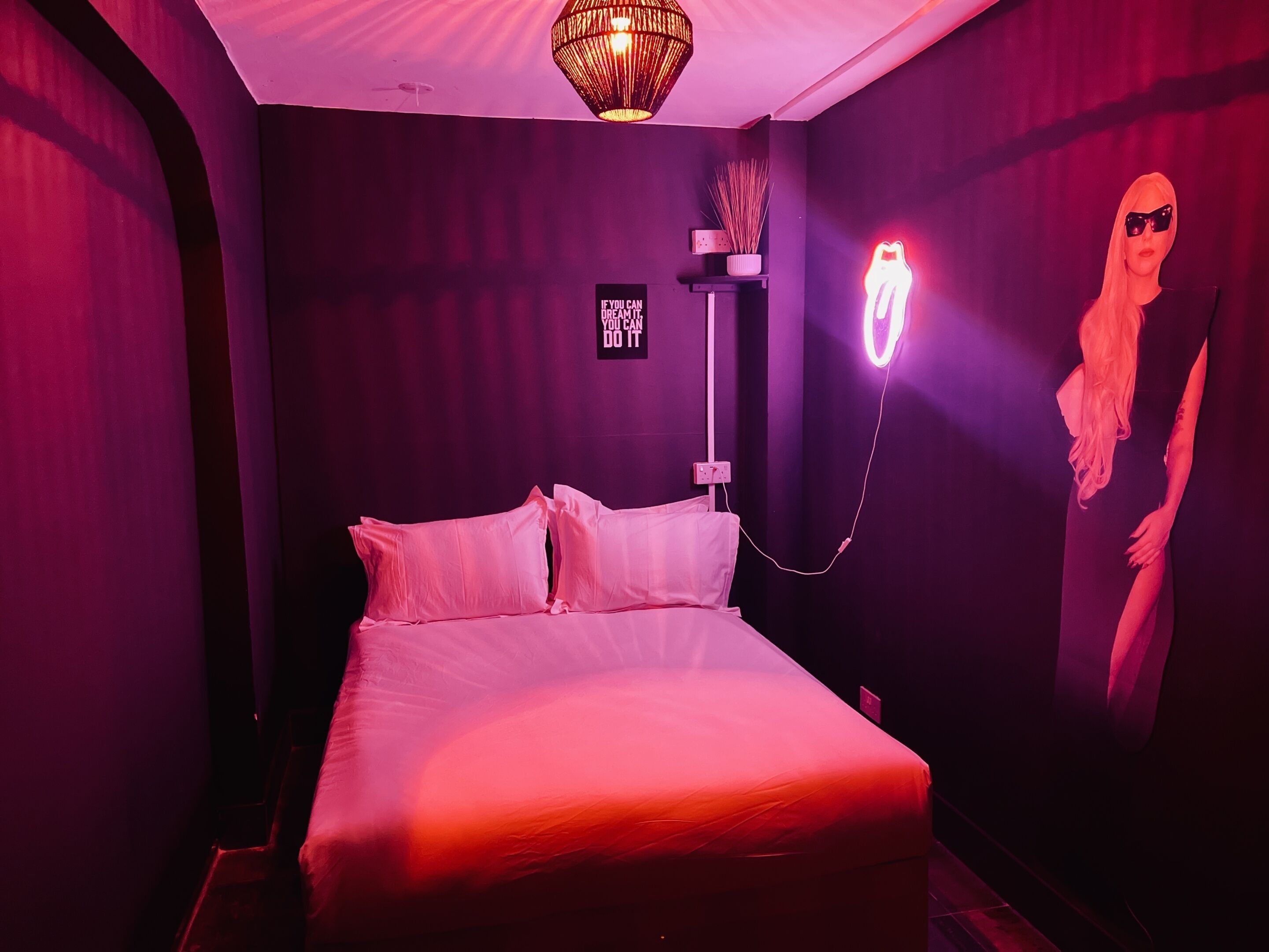 A room with a bed, a wall-mounted light fixture, and a neon sign.