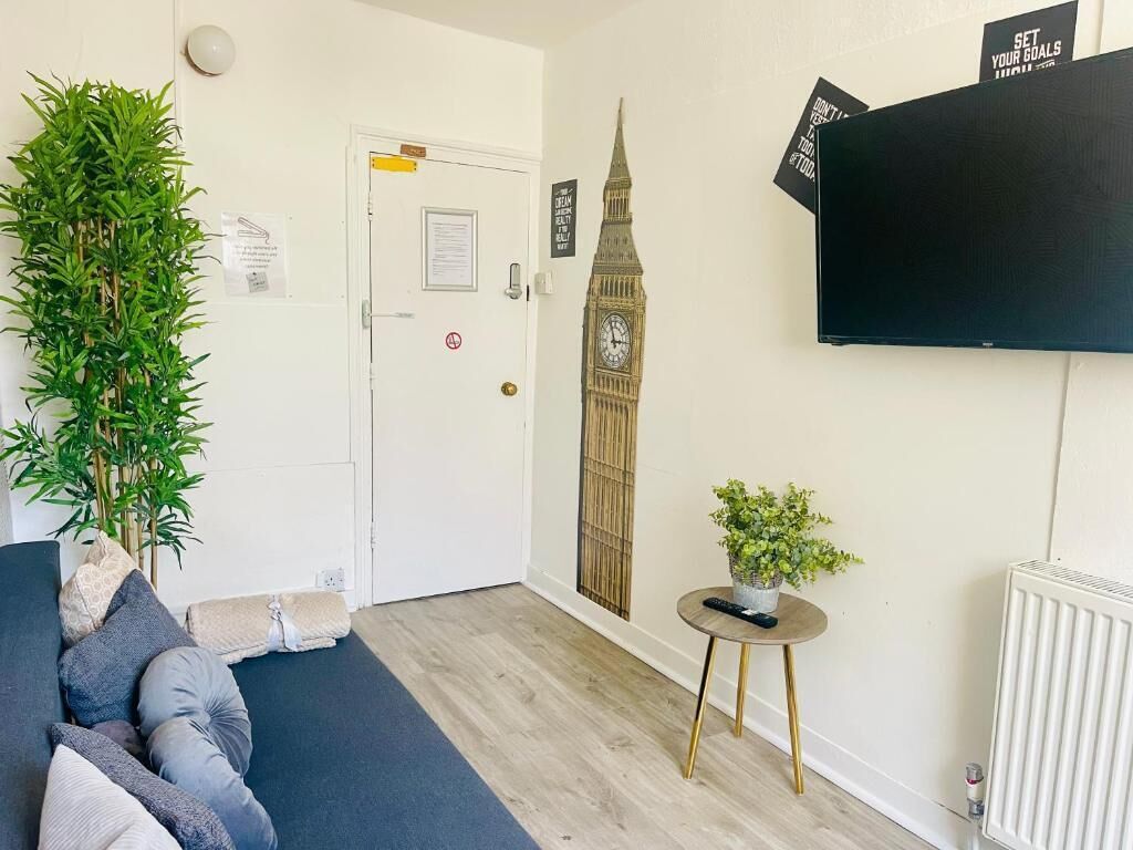 Ein Zimmer mit einer Couch, einem Blumentopf, einem an der Wand befestigten Fernseher, einem Heizkörper und einer Tür mit einem Hinweisschild.