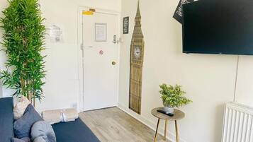 Ein Zimmer mit einer Couch, einem Blumentopf, einem an der Wand befestigten Fernseher, einem Heizkörper und einer Tür mit einem Hinweisschild.