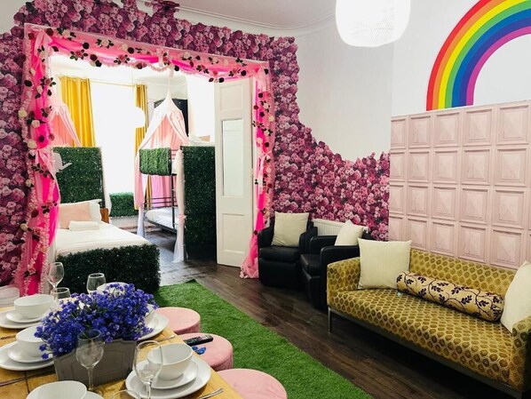 A room with a bed, a sofa, a dining table set with plates and glasses, and a wall with a floral pattern.
